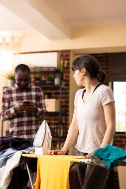 Kız arkadaşı öfkeyle erkek arkadaşına bakıyor ve temiz çamaşırları yıkıyor. Beyaz kadın kıyafetlerini ütülüyordu. Kocası evde durduğu gibi cep telefonu kullanıyordu. Eşit olmayan ev işlerini gösteriyordu.