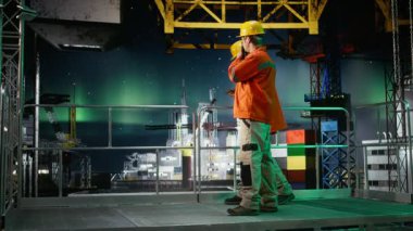 İşçi aurora borealis altındaki kıyı petrol platformunda radyo istasyonları aracılığıyla iletişim kurarak, emisyonları azaltmak ve deniz habitatlarının çıkarılmasını desteklemek için sondaj sondaj sondajı sistemlerini yönetiyor. Kamera A.