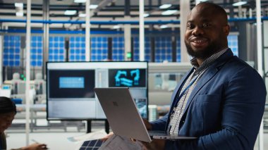 Fabrikada gülümseyen mühendisin portresi parametreleri kontrol etmek ve güneş panelinin dayanıklılığını artırmak için dizüstü bilgisayar kullanır. Mutlu Afrikalı Amerikalı araştırmacı verimli sürdürülebilir enerji çözümleri geliştiriyor, kamera A