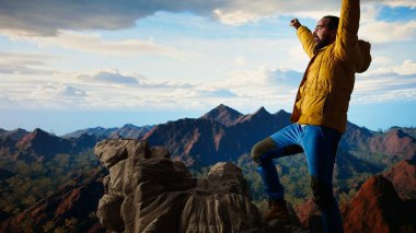 Trekker kollarını dağ sırasının tepesinde heyecan içinde uzatıyor, tırmanma başarısından gurur duyuyor ve tatmin oluyor. Genç yetişkinler azim ve hırslarını sergilerler. Kamera A.