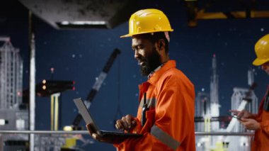 Kara kıyı mühendisi dizüstü bilgisayar kullanarak petrol sondaj platformunu izliyor ve doğal gaz ve petrol çıkarmasını kolaylaştırmak için verimli endüstriyel faaliyetler sağlıyor. Fosil yakıt pompalıyor. Kamera B.