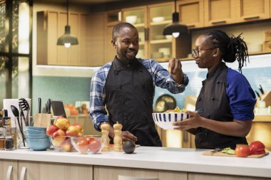 Mutlu çift parlak bir mutfakta taze bir salata hazırlıyor, bir tutam tuz ekliyor ve kadın renkli sebzeleri bir kaseye karıştırıyor. Vejetaryenlerin sağlıklı yaşam tarzı.
