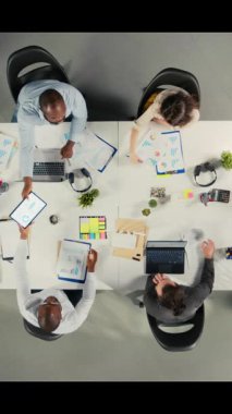 Çok uluslu şirketteki iş ekibinin dikey video üst görüntüsü ölçümleri ve projeksiyonları analiz ediyor. Personel, iş hedeflerini desteklemek için strateji planlaması ve rapor paylaşımı konusunda işbirliği yapmaktadır. Kamera A.