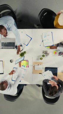 Bir şirket toplantısında finans ve bütçe konularında danışmanlık yapan iş adamlarının düşey videosu. Personel, hedefleri ve planlama stratejilerini belirlemek için belge, diyagram ve raporları analiz eder