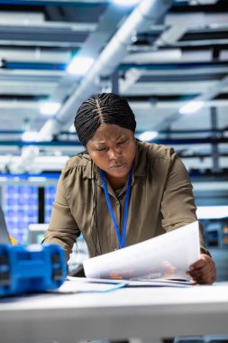 Afrikalı Amerikalı analist güneş enerjisi kalitesini bir tesiste değerlendiriyor, sürdürülebilir güneş enerjisi için kusursuz üretim hattını sağlamak için veri raporlarını ve içgörülerini gözden geçiriyor. Fotovoltaikler.