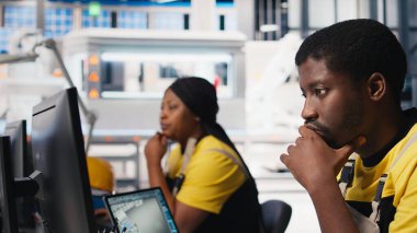 Erkek uzman makine parametrelerini güneş paneli üretimi için ayarlıyor, yüksek teknoloji üretim tesisinde çalışıyor. Siyah mühendis bilgisayarda teknik verileri analiz ediyor. Kamera B.