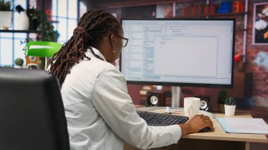 İş istasyonundaki programlamada kodlayıcı, kod satırları yazmak, geliştirme araçları kullanmak, stres hissetmek. Ofisteki kadının son teslim tarihi var, hata ayıklama yazılımını bitirmek için stresli, kamera B