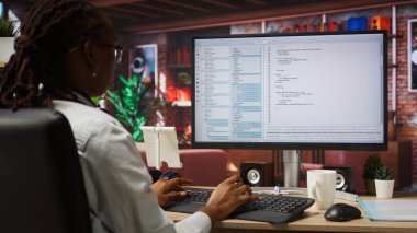 Bilgisayar masası kodlamasında programcı, yazılım yaratıyor, algoritmalar uyguluyor. Afrika kökenli Amerikalı bilişim uzmanı. Kod editörü, bina uygulamaları, kamera A ile çalışıyor.