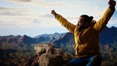 Zirvede duran kararlı dağcı huzurlu bir başarı anının tadını çıkarıyor. Uçsuz bucaksız gökyüzü, dağ sıraları ve temiz hava özgürlüğün, refahın ve keşiflerin özünü vurguluyor. Kamera A.