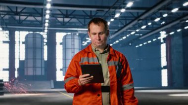 Müfettiş, üretimi koordine etmek için tablet kullanarak bir depodaki makine operasyonunu denetliyor. Güçlü insan gücü, mühendislik disiplini ve endüstriyel performans gösteriyor. Kamera B.
