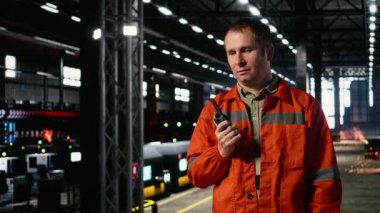 Teknisyenlerin elinde metal ekipman ve inşaat araçlarıyla çevrili endüstriyel çevredeki bir üretim tesisinde telsiz var. Kamera A.