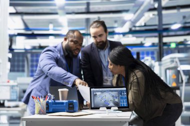 Multiethnic team of technicians collaborating in a solar panel power plant, reviewing blueprints and sharing ideas to enhance renewable energy production and sustainable innovation.