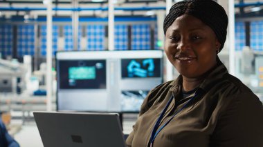 Araştırmacının portresi güneş pili prototiplerini enerji üretimini optimize etmek için dizüstü bilgisayar kullanarak analiz eder. Gülümseyen Afro-Amerikan güneş panelleri yenilikçi üretim teknolojisi geliştiren bitki uzmanları, kamera A