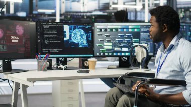 Veri merkezinde belden aşağısı felçli mühendis yapay zeka ağacı yazılımı hatası yüzünden panikledi. Tekerlekli sandalyedeki endişeli sunucu merkezi çalışanı görsel programlama aracı arızası yüzünden endişeli, kamera B