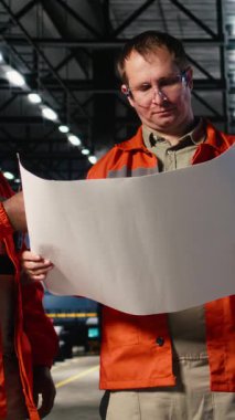 Dikey Video Çeşitliliği mühendisleri montaj işlerini endüstriyel planlarla yürütüyor, çelik makineleri ve ağır sanayi gelişimini temsil eden üretim istasyonlarının yanında duruyorlar. Kaynak kıvılcımları