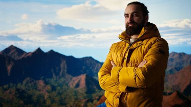 Heyecanlı maceracı, azim ve dayanıklılık ruhunu somutlaştırarak dağın zirvesine ulaşmasını kutluyor. Yürüyüşçü bir dağ silsilesinin panoramik manzarasının tadını çıkarıyor. Kamera A.