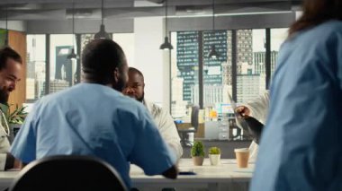 Tıbbi uzmanlar teşhis ve tedavi üzerine klinik bir tartışmaya katılıyorlar. Doktorlar ve hemşireler sağlık verilerini analiz eder ve hasta bakımı stratejilerini koordine ederler. Kamera B.