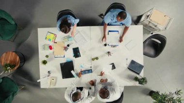 Sağlık ekibinin hasta bakımını incelemek ve görüşlerini paylaşmak için düzenlediği bir toplantıda çalışan sağlıkçılara yukarıdan bak. Tedavi planlama ve klinikte ilerlemeye odaklanıyor. Kamera A.