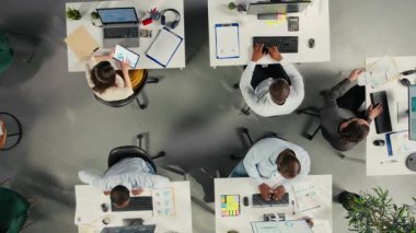 Modern ofiste çalışan, proje planlama, performans ölçümleri ve rapor paylaşımına odaklanan çeşitli meslektaşların yukarıdan aşağıya yakınlaşması. İş adamları hava tahminleri için verileri gözden geçiriyorlar. Kamera A.