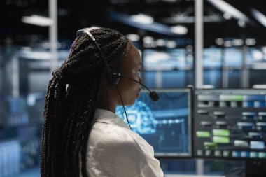 Veri merkezindeki sistem yöneticisi kulaklık mikrofonuyla konuşuyor, kullanıcı teknik desteği sağlamak için yapay zekayı kullanıyor. Uzaktan arama sırasında sunucu odasında müşterilere yardım eden Afrikalı Amerikalı bir kadın.