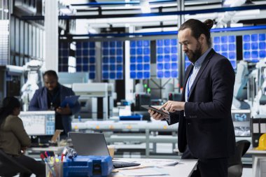 Bir güneş paneli tesisinde çalışan erkek üretim teknisyeni sistem performansını değerlendiriyor ve verimlilik ve işyeri güvenliğinin izlenmesinde önemli bir rol oynuyor. Yenilenebilir güç kavramı.