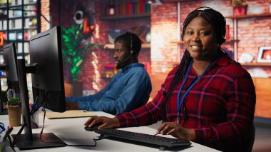 İyimser çağrı merkezi temsilcisi müşterilere rehberlik ediyor, soruları cevaplıyor. Jolly Afrikalı Amerikalı müşteri merkezi çalışanı PC masasında müşterileri arama sırasında teknik çözümler üzerinden yürütüyor, kamera B