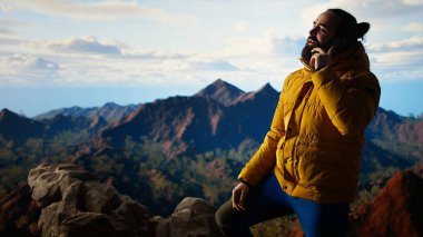 Trekker yüksek rakımlı manzaranın tadını çıkarıyor ve bir telefon görüşmesi yapıyor, panoramik dağ manzarası ve gevşek hava rahatlama için mükemmel bir manzara sağlıyor. Akıllı telefonunda güçlü bir sinyal kullanıyor. Kamera A.
