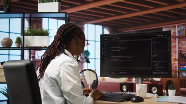 Müzik dinlerken, yazılım yaratırken, algoritmalar uygularken bilgisayar masası kodlaması geliştiricisi. Uzaktan çalışan, kulaklıklı, kod düzenleyici, bina uygulamaları, kamera A ile çalışan biri.