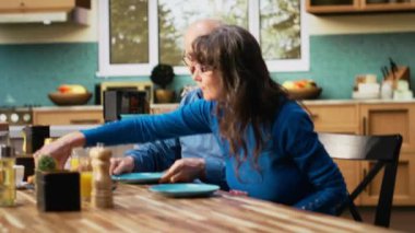 Olgun bir çift kahvaltı servisi yapıyorlar. Hamur işi, sıcak kahve, parlak mutfak masası. Sakin bir sabah rutini ve rahat bir emeklilik hayatı içinde sohbet ve kaynaşma. Kamera B.