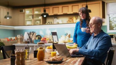 Üst düzey emekli insanlar, sabah rutin tarama dizüstü bilgisayarlarında ev yapımı kahvaltının masada taze kahve ve hamur işi servis edilmesinin keyfini çıkarıyorlar. Karı koca gündelik bir konuşma yapıyorlar. Kamera A.