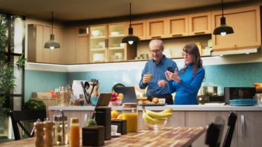 Yaşlı ev hanımı mutfaktaki tezgahın yanındaki cep telefonuyla evde sakin bir anın tadını çıkarıyor. Huzurlu bir yaşam tarzı, sağlıklı bir yaşam ve emekli olmanın keyifli rahatlığını yansıtıyor. Kamera A.