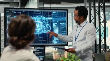 Şirket sistem performansını optimize etme sunumunu göstermek için yönetici tarafından kullanılan ekran. Açılış ofisindeki işçiler suni zeka, kamera B üzerine açılış konuşması yapmak için görüntü kullanırlar.