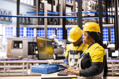 Sanayi 4.0 uzmanları dijital kontrol panelini çalıştırıyor, otomasyon hattını optimize ediyor ve robotik kol doğruluğunu sağlıyor. Afrikalı Amerikalı teknisyenler akıllı üretim tesisinde üretim akışını yükseltiyorlar.