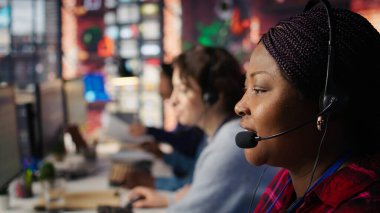 Çağrı merkezi çalışanı mikrofonla konuşur, müşteri soruşturmaları ve şikayetlerle ilgilenir. Afrika kökenli Amerikalı müşteri hizmetleri temsilcisi müşterilere sorunlarda yardımcı oluyor. Kamera B, kapat.