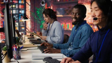 Gülümseyen teknik destek uzmanının portresi çağrı merkezinde sorun çözüyor. Neşeli Afro-Amerikan IT çalışanı müşteri bağlantılarını düzeltiyor, kulaklık kullanıyor, kamera B