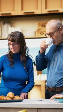 Dikey Video Yaşlıları, ev mutfağında dizüstü bilgisayarda gezinen ve bir fincan kahve ve huzurlu rahatlama keyfi yapan bir çift ile evlendi. Neşeli bir yaşam tarzı, mutlu ve rahat anlar.