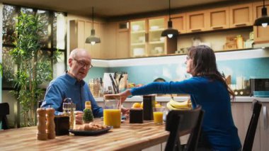 Yaşlı çift, sağlıklı ev yapımı kahvaltıyla, hamur işi yiyerek ve kahve içerek doğal sabah rutininin tadını çıkarıyor. Karı koca samimi bir an için gündelik bir konuşma yapıyorlar. Kamera A.