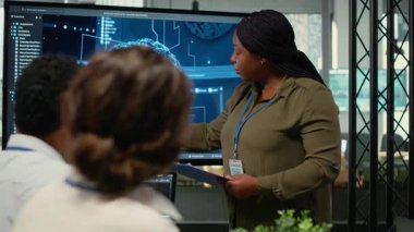 Yatırımcılar için sunum yapan teknoloji firması yöneticisi toplantı odasında toplandı. Yapay zeka sektöründeki son yenilikleri iş adamlarının önünde sergileyen Afrikalı Amerikalı kadın, kamera B