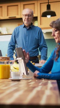 Daire mutfağındaki neşeli yaşlı adamın dikey video portresi emeklilik süresince rahatlamış bir zevk gösteriyor. Yaşlı kişi tezgahın yanında durur, günlük ev bakımını ve olumlu ev refahını kucaklar.