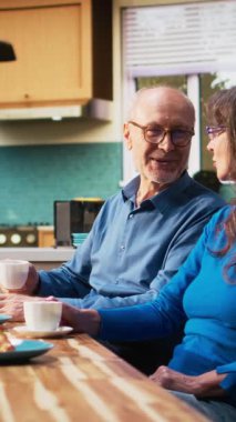 Dikey video yaşlanan karı koca kahve fincanlarıyla tatlı anlar yaşıyor, birbirlerine bakıyor ve sabahları sohbet ediyorlar. Huzurlu emeklilik, pozitif yaşam tarzı ve ev hayatının keyfi.