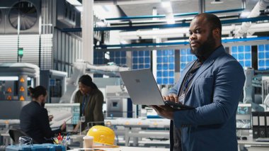 Bir güneş paneli tesisinde Afrika kökenli Amerikalı yönetici performans ve verimlilik ölçümlerini izliyor, gerçek zamanlı kalite kontrolü ve stratejik iş geliştirme ile liderliği birleştiriyor. Kamera A.