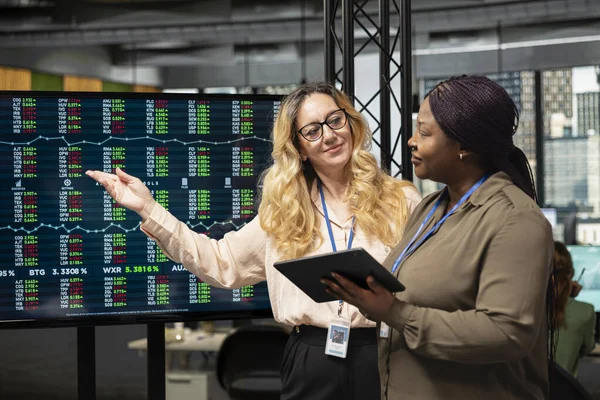 Tahmini raporlar veya başarı ölçümleri sunabilecek stratejik bir sunum üzerinde işbirliği yaparak, toplantı odasındaki TV monitöründeki verileri gözden geçirmek için yan yana çalışan çeşitli iş kadınları.