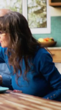 Dikey Video Üst Düzey çifti kahvaltıda rahat bir sabah rutininin tadını çıkarıyor. Karı koca samimi bir anı paylaşıyor ve mutfak tezgahında gülüyor, sıcak kahve eşliğinde sağlıklı yiyecekler servis ediyorlar.