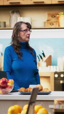 Dikey video yaşlı çift kahve ve neşeli gülümseme ile ev mutfağında duruyor, günlük ev işleri ve sağlıklı yemek anlarının keyfini çıkarıyorlar. Huzurlu bir yaşam tarzı, sıradan bir hayat ve tatmin edici bir yaşam.