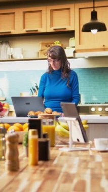 Sakin bir mutfakta, sakin bir yetişkin videosu dizüstü bilgisayarında kaydırma uygulamaları kuruyor ve huzurlu bir emeklilik hayatı yaşıyor. Nazik bir gülümseme gösteren kadın, rahat bir aile hayatı yansıtan basit anlar.