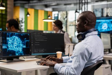 Bilgisayarda yapay zeka teknolojisi kullanarak sürekli iş akışlarını otomatikleştiren bir bilgisayar çalışanı. Afrikalı Amerikalı adam bilgisayarla derin öğrenme hesaplama modellerini inceliyor.