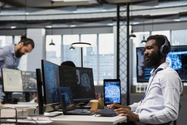 Yapay zeka öğrenme sistemlerini ofiste birleştiren, müzik dinleyen bir teknoloji şirketi. Kulaklık takan mühendis sinirsel ağlar kullanıyor. Yapay zeka, teknoloji aşırı yükleme kavramı.