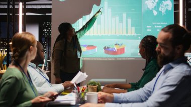 Çeşitli şirket ortakları proje zaman çizelgelerini ve gündemi inceler, konferans odasında saatler sonra kalkınma için bir strateji oluştururlar. İş ortamında hedef belirleme. Kamera A.