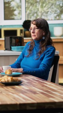 Dikey Video Yaşlanan olgun bir kadın erkeğini görmezden geliyor ve masada kendinden geçiyor, ilgisiz bir eş oturuyor ve kafası meşgul. Kahvaltı sırasında dikkati dağılmış ve dağılmış. Kamera B.