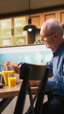 Ekmek kızartma makinesi ve ev yapımı yemekle kahvaltı servisi yapan Dikey Video Üst Düzey Yaşlılar, evde huzurlu bir sabah rutini paylaşıyorlar. Emeklilik çağında kahkahalarla ve gündelik sohbetlerle sıcak bir an. Kamera.